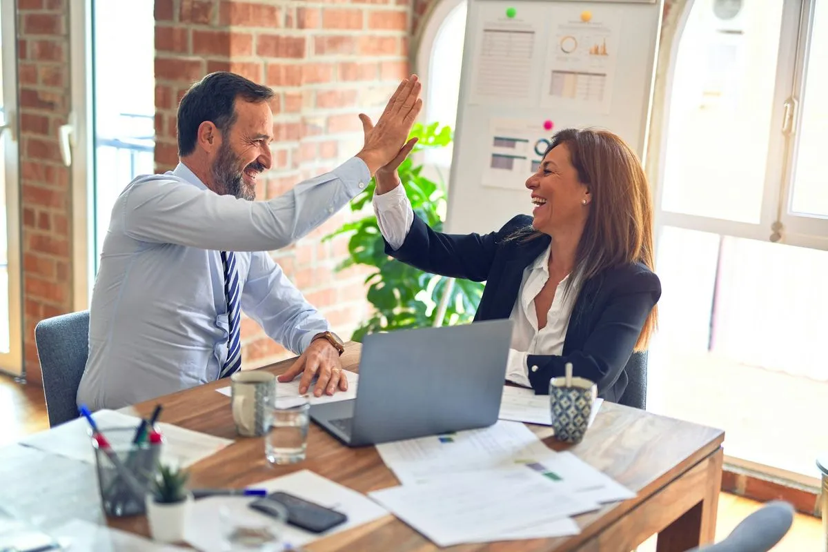 Twee collega's die elkaar enthousiast een high five geven achter een laptop